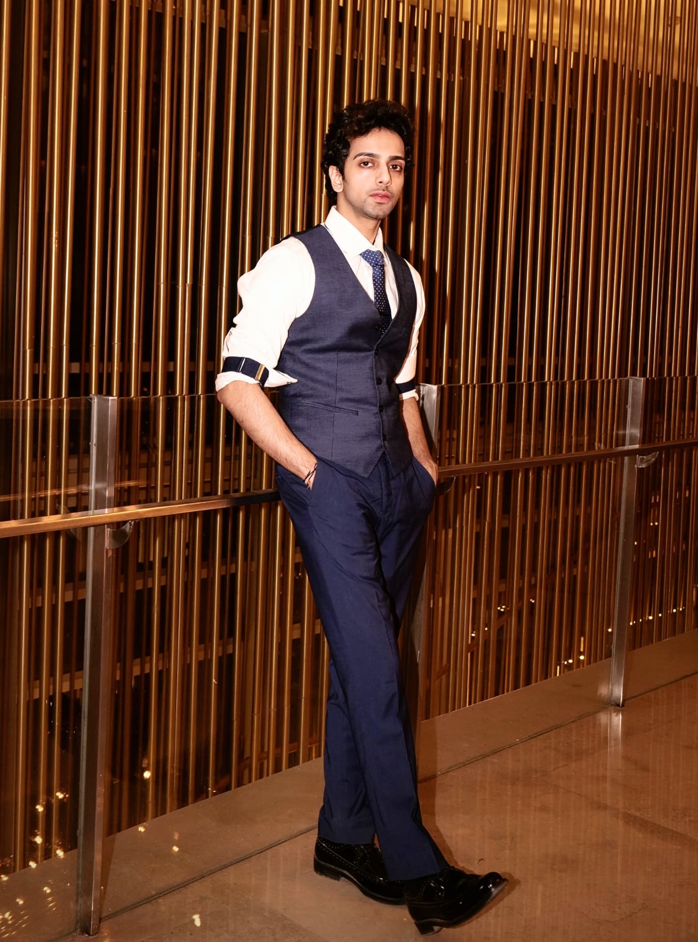 Sabyasachi Moulik in a navy three-piece suit against a gold slatted wall